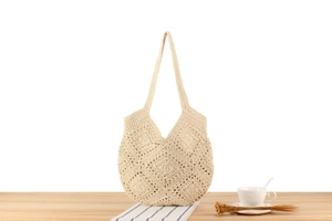 Close-up of cream handmade crochet tote bag with hollow floral texture on wood