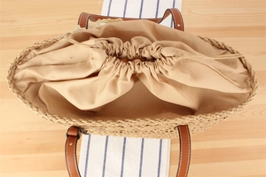 Close-up of woven straw bag interior with drawstring lining and leather handles