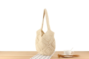 Detail of cream crochet tote bag with openwork floral pattern on a wooden table
