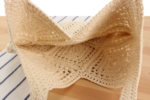 Detailed top view of beige crochet tote bag with geometric knit patterns on a striped cloth