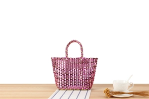Détail du mini sac tissé main en rose métallisé et doré sur un chemin de table rayé