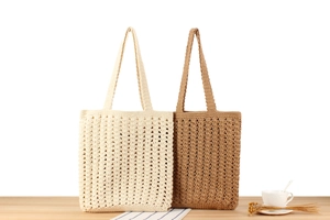 Detail view of hollow crochet tote bags in cream and khaki on a light wooden table