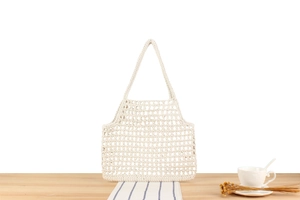 Detail of hollow-out cotton crochet tote bag on a wooden table with a white coffee cup