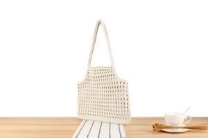 Detailed close-up of cream woven cotton handbag with openwork texture and wood handle