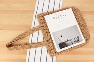 Flat lay of a hollow-out woven cotton tote bag on a wooden table with a minimalist book
