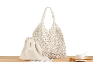 Detail of woven mesh shoulder bag with a canvas drawstring inner pouch on wood surface