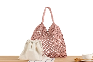 Close-up of pink macrame woven bag with white cotton drawstring lining on wooden desk
