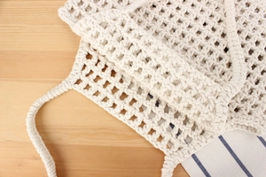 Detailed macro view of white hollow cotton woven bag texture on light wooden background