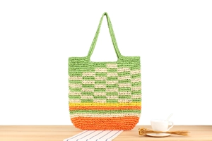 Detail of multi-color woven straw tote bag on wooden table with a coffee cup