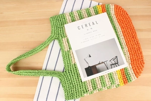 Detail of color-block striped paper rope woven tote bag on a rustic wooden table