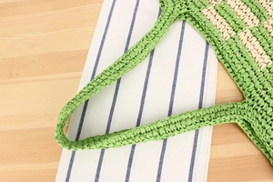 Detail of green and beige paper rope woven bag with striped texture and handle