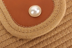 Détail d'un sac en paille tressée avec ornement perle et empiècement en cuir marron