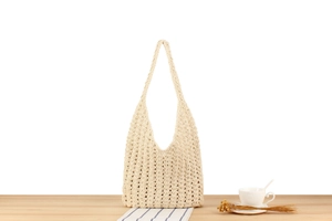 Close-up of beige woven cotton shoulder bag with hollow wave texture on a wooden table