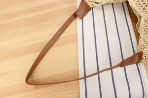 Detail of paper straw woven bag featuring a brown leather strap with precise stitching