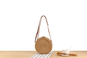Detailed view of woven paper rope circular crossbody bag with leather strap on table