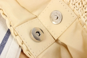 Close-up of a silver magnetic snap button on the fabric lining of a woven paper bag