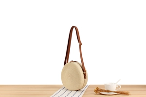 Close-up of a woven straw circle crossbody bag with adjustable brown leather strap