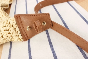 Detail of paper straw woven strap with brown leather trim and golden metal rivets