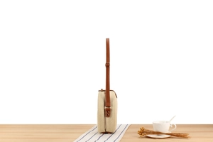 Detail of beige woven straw shoulder bag with adjustable brown leather strap on a table