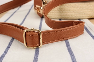 Detail of brown leather strap with gold metal buckle on a beige woven straw bag