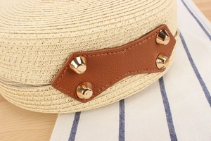 Close-up of beige woven round bag featuring brown leather patch and gold metal rivets