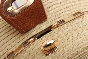 Macro detail of paper rope woven bag featuring brown leather strap and gold zipper pulls