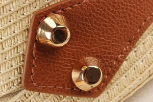 Macro shot of ivory woven raffia material with brown pebbled leather and gold metal studs