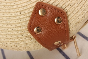 Detail of woven straw crossbody bag with brown leather patch and gold metal rivets