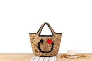 Detail of woven straw handbag featuring a black smiley face and red heart eye design