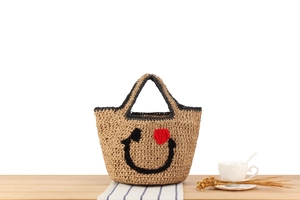 Detail of straw tote bag with smiling face embroidery and red heart eye detail