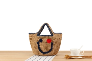 Detail of woven straw handbag featuring smiley face embroidery and blue handles