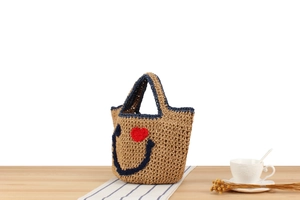 Close-up of handmade woven straw tote with navy smiley face and red crochet heart detail