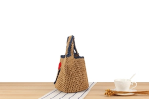 Detail of hand-woven straw tote with navy blue trim and red crochet heart accent