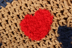 Close-up detail of woven texture and fuzzy red heart patch on casual straw beach bag