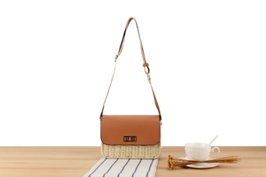Detail of woven straw shoulder bag with brown leather flap and golden metal clasp lock