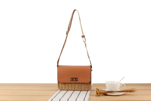 Detail of woven straw and brown leather crossbody bag with a gold metal turn-lock buckle