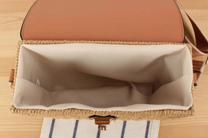 Top view of woven paper rope bag interior with brown leather flap and metal turn-lock