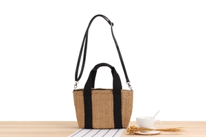 Détail d'un sac cabas beige en paille de papier avec anses noires et bandoulière