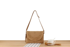 Detail of hand-woven straw envelope crossbody bag with decorative trim on wood surface