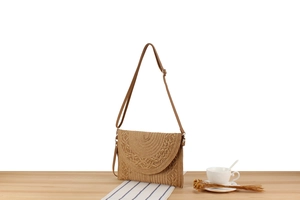 Detail of hand-woven paper rope crossbody bag with textured flap and metal hardware