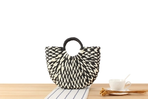 Detail of black and white woven paper rope handbag with circular handle on a table