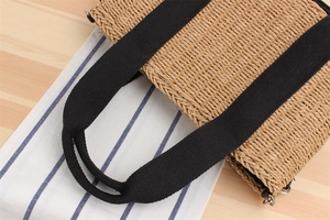 Détail d'un sac cabas en paille avec anses en toile noire sur fond en bois clair
