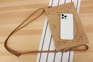 Flat lay of a woven straw envelope bag with leather straps on a wooden background