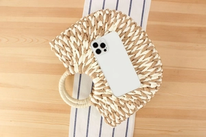 Detail of a semi-circular woven straw handbag with a round handle next to a phone for scale