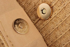 Macro detail of golden magnetic buckles on hand-woven paper straw crossbody bag