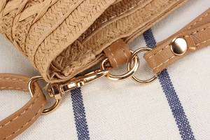 Detailed close-up of straw woven crossbody bag with brown leather accents and gold hardware