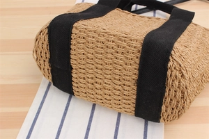 Détail latéral du sac cabas en paille tissée avec sangles en toile noire et base solide