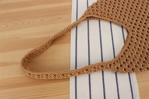 Détail d'un sac bohème en coton tressé kaki avec maille ajourée sur fond de bois