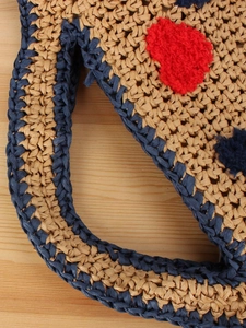 Straw woven tote with heart patch and blue trim details on a light wooden surface