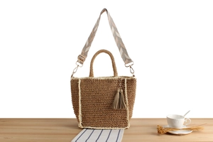 Detail of hand-woven straw tote with geometric strap and leather tassel on a wooden desk